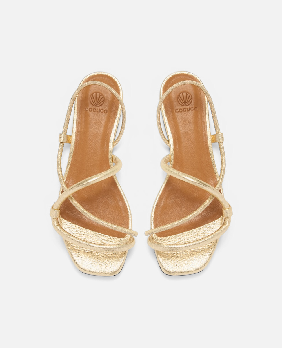 Top view of a crinkled metallic gold flat sandal with slim cylindrical padded straps and an elasticated slingback, square toe, on a white background.