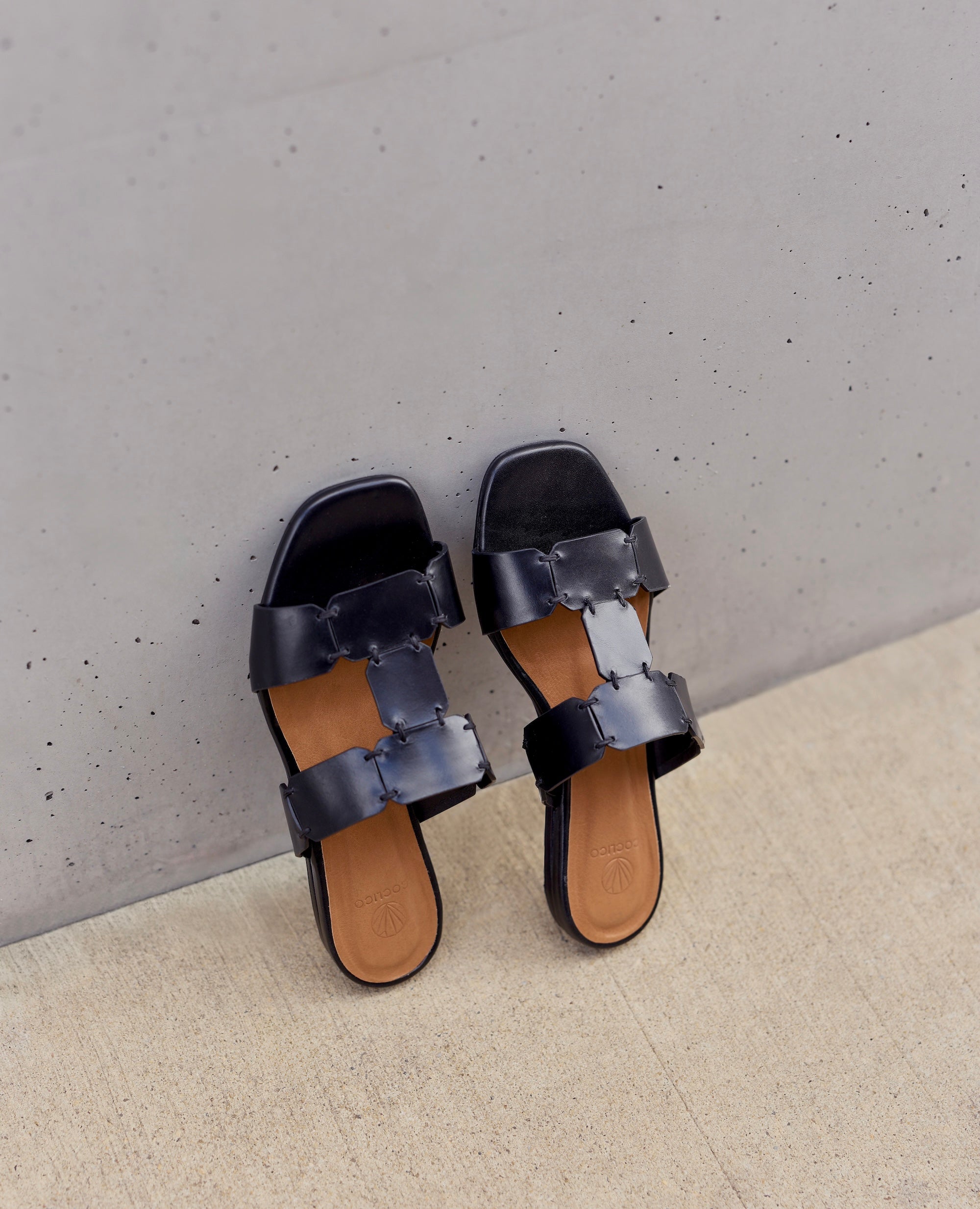 Pair of black sandals on a light gray wall.