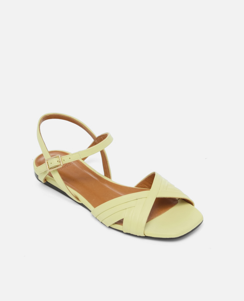 Angled view of a pale yellow leather flat sandal with slim crisscross toe straps, buckle quarter strap, and square toe, on a white background.