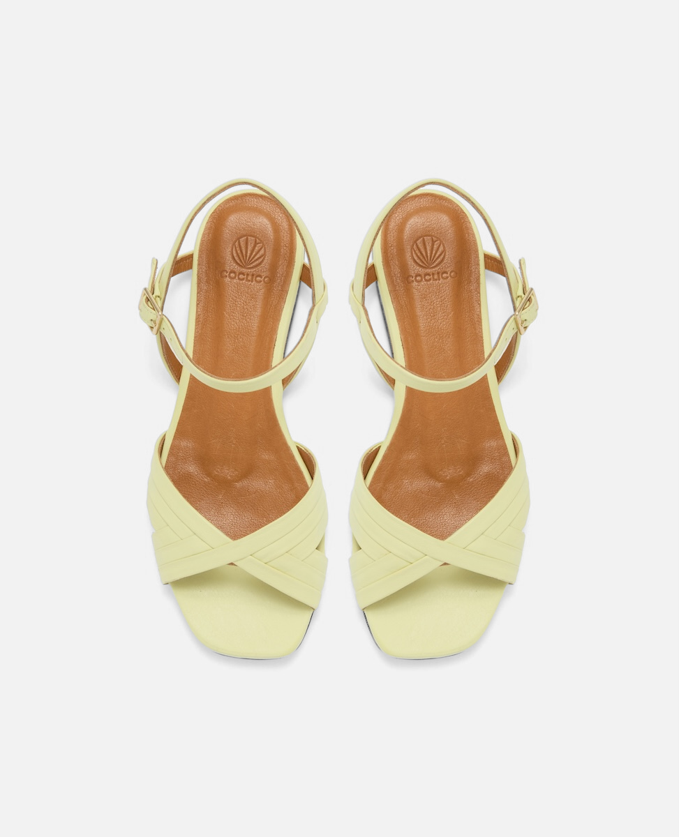 Top view of a pale yellow leather flat sandal with slim crisscross toe straps, buckle quarter strap, and square toe, on a white background.