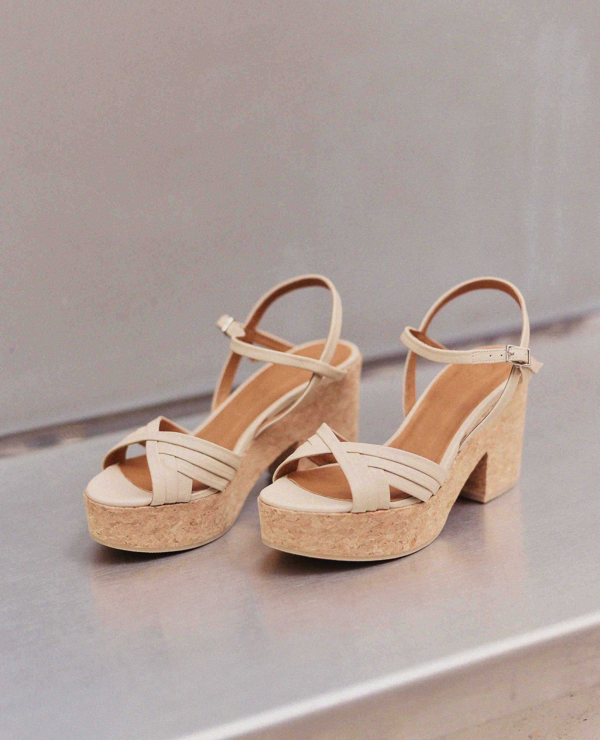 Pair of beige cork platform sandals on a reflective surface with a neutral background