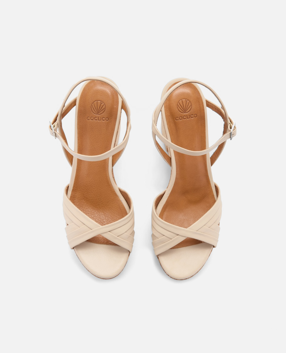 Beige open-toe sandals with crisscross straps, a slim ankle strap with a buckle, and a smooth leather finish.
