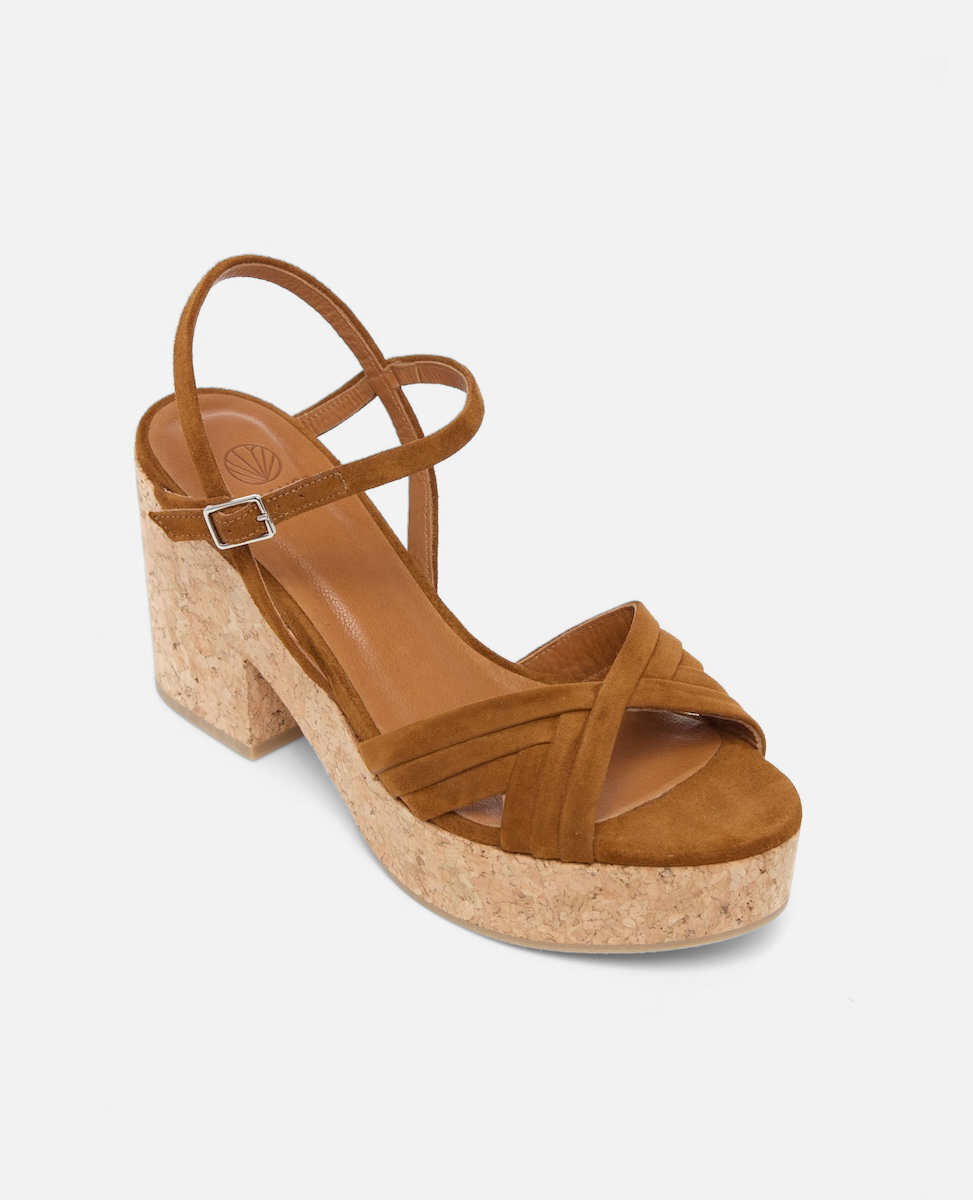 A brown suede sandal with a cork block heel, featuring crisscross straps over the toe and an adjustable ankle strap.