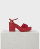 A vibrant red sandal with a chunky block heel and platform, featuring a smooth, glossy finish, two wide straps across the front, and an adjustable ankle strap, all set on a textured, marbled sole. 1