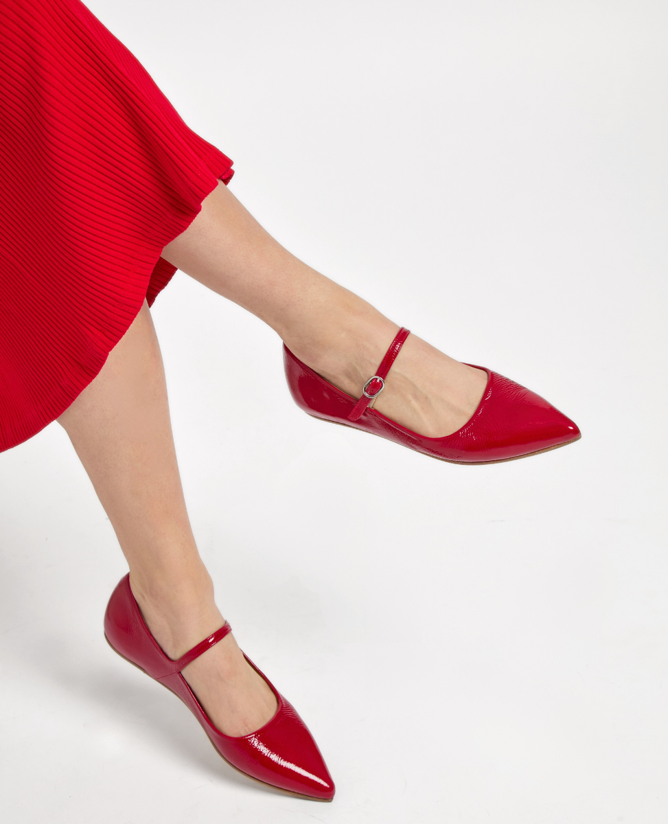 A pair of shiny red patent leather Mary Jane flats with pointed toes, a slim ankle strap with a small buckle, and a smooth, glossy texture.