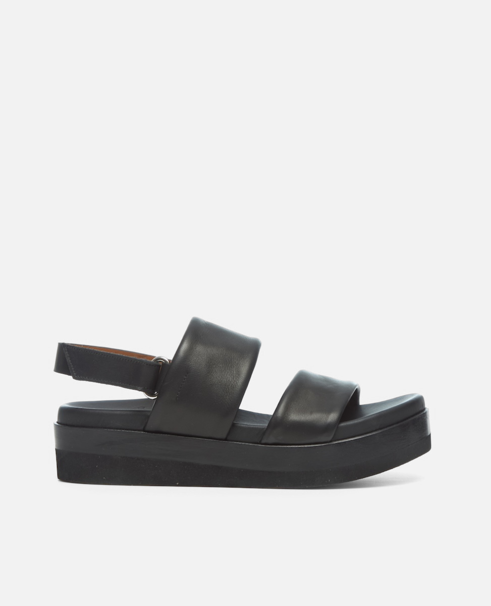 A black sandal with a thick platform sole, featuring two wide leather straps across the foot and an adjustable ankle strap, showcasing a sleek and minimalist design.