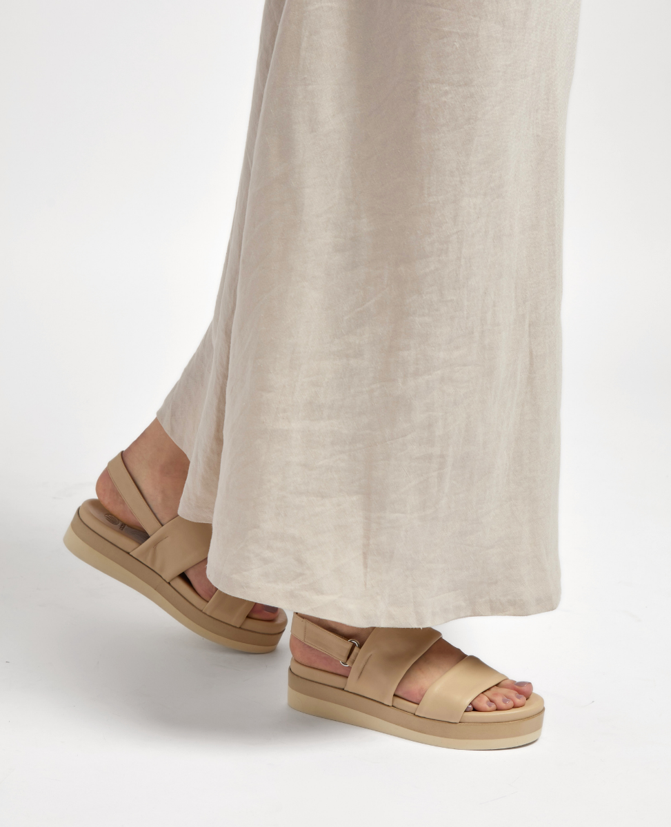 Beige platform sandals with wide straps and a buckle detail, featuring a smooth leather texture and a thick, cushioned sole.