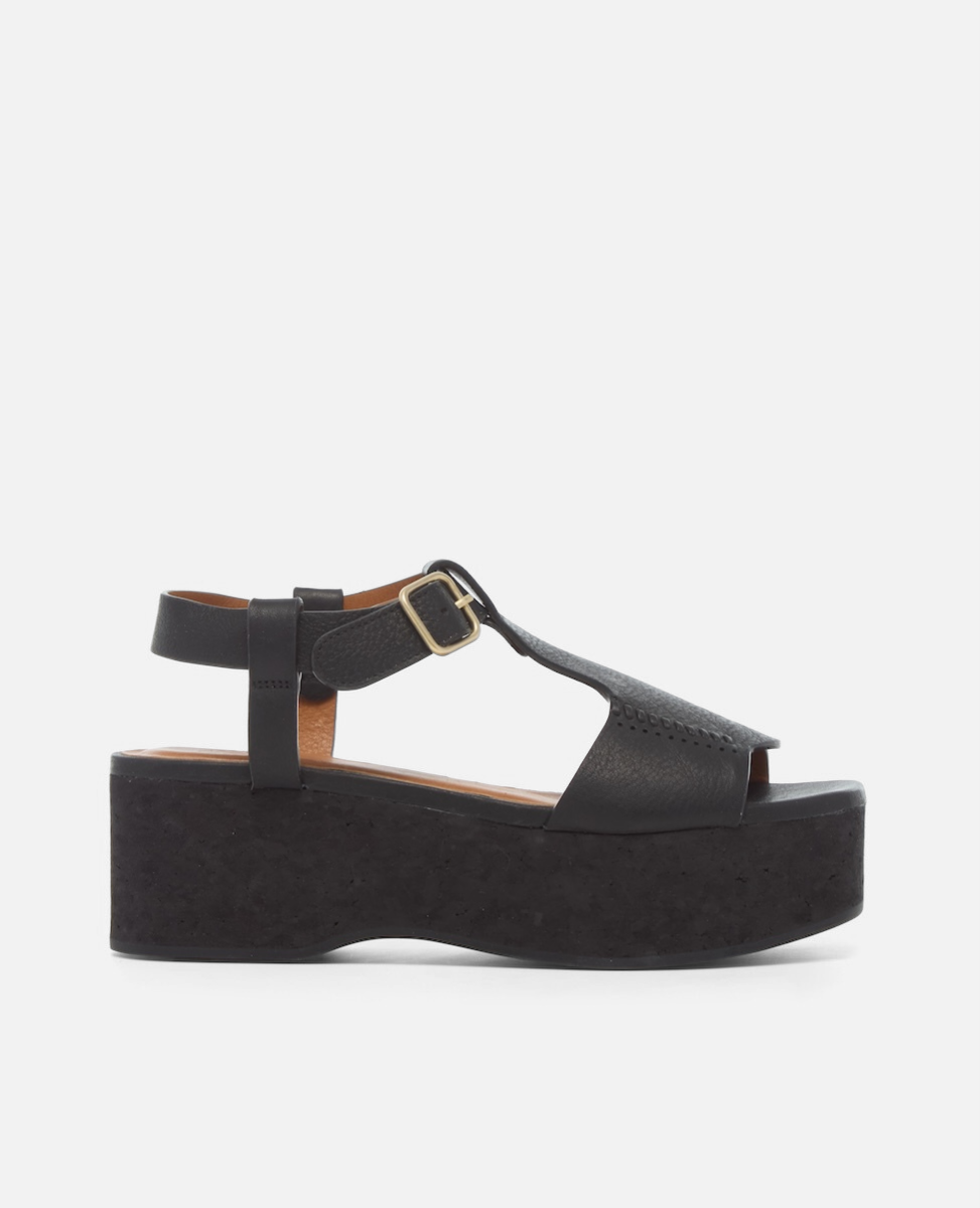 Side view of a black leather wedge sandal with wide stitched straps, adjustable ankle buckle, and a black-stained cork platform sole