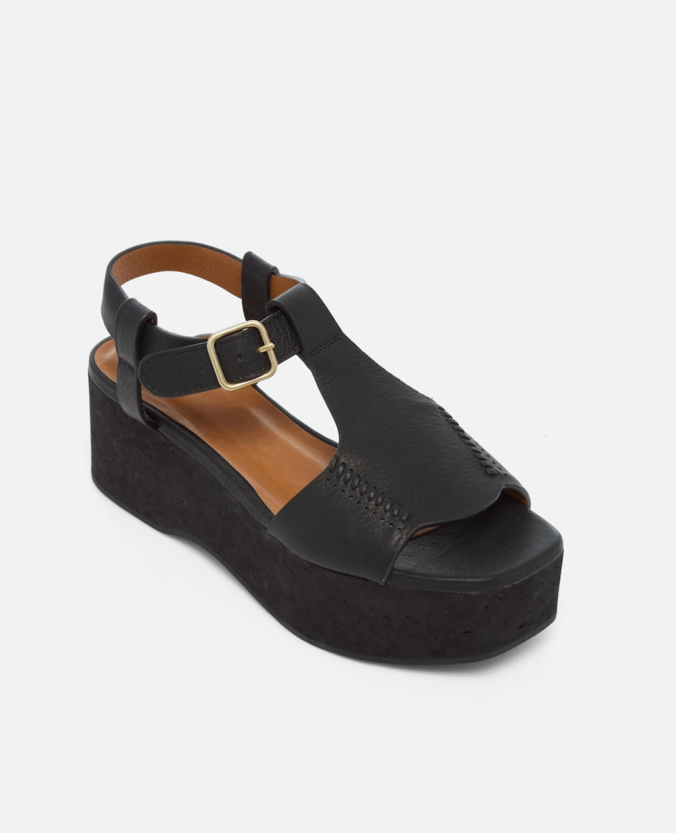Angled view of a black leather wedge sandal with wide stitched straps, adjustable ankle buckle, and a black-stained cork platform sole