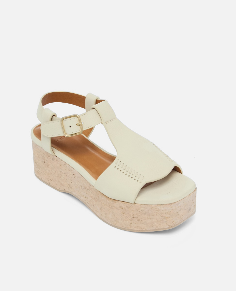 Angled view of a white nubuck leather wedge sandal with wide stitched straps, adjustable ankle buckle, and a whitewashed cork platform sole