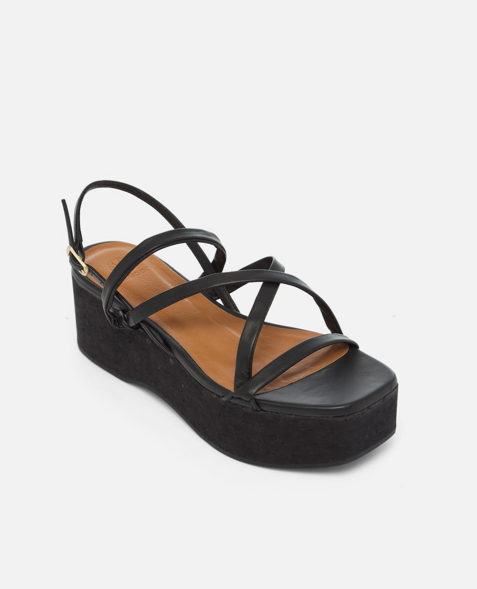Angled view of a black leather cork wedge sandal with slim crisscross straps, adjustable slingback, and a sculptural cork platform sole