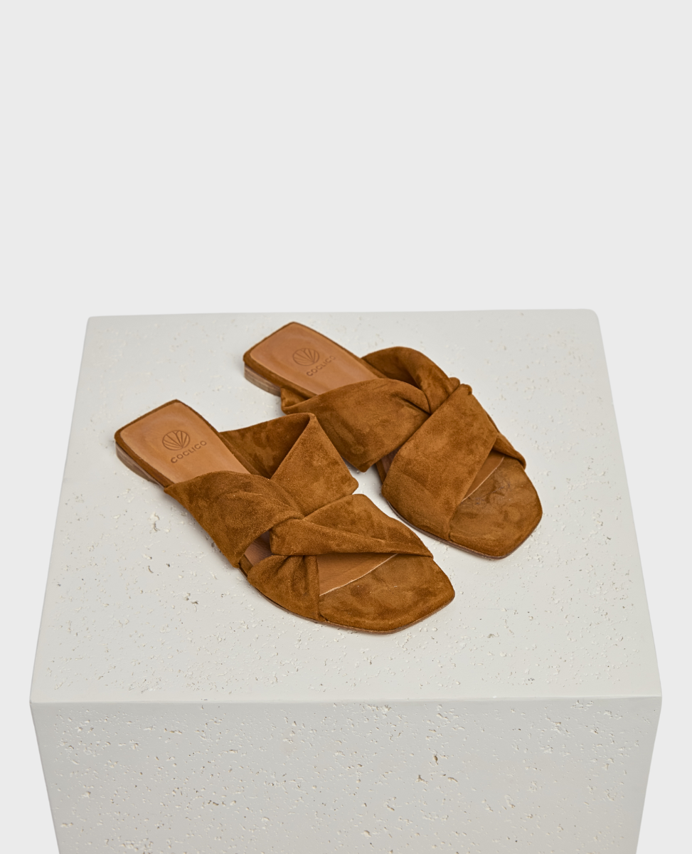 Brown suede sandals with a flat sole, featuring a crisscross strap design and a square open toe.