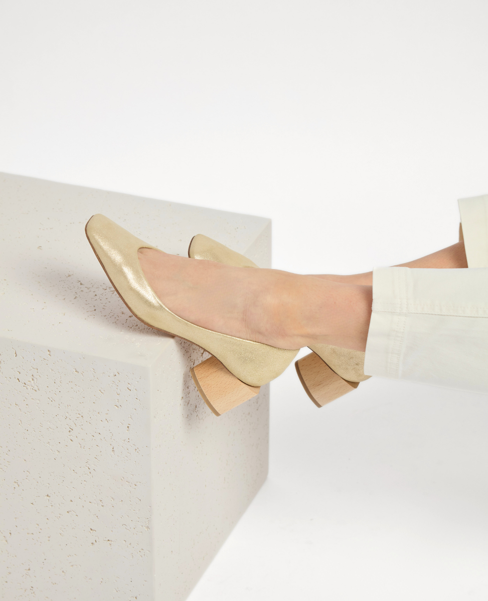 A pair of elegant, gold-colored, low-heeled shoes with a smooth, shiny texture and a rounded toe, featuring a wooden block heel and a slip-on design.