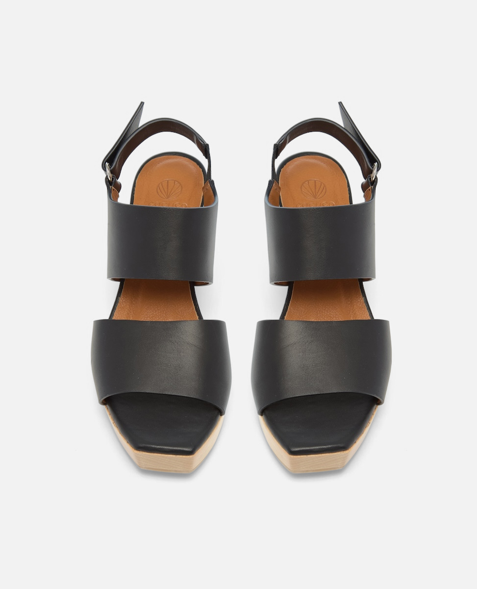 Black leather clog sandals with wide straps, a tan insole, a square open toe, and a buckle closure at the ankle.