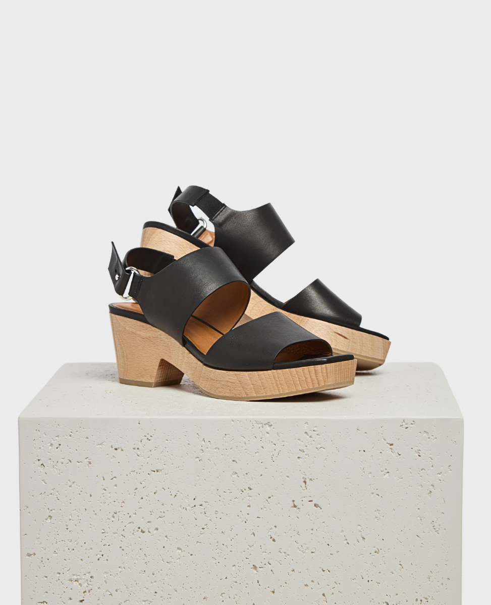 Black leather sandals with a chunky wooden heel, featuring a peep-toe design and an adjustable ankle strap with a silver buckle.