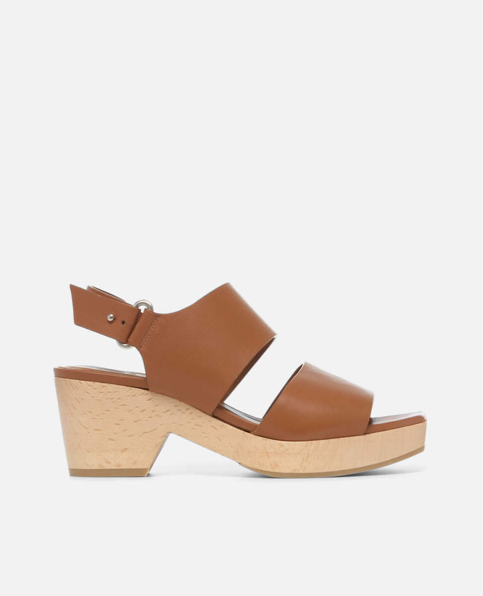 A brown leather clog sandal with a wide strap design, featuring a wooden wedge heel and an adjustable ankle strap with a silver buckle.