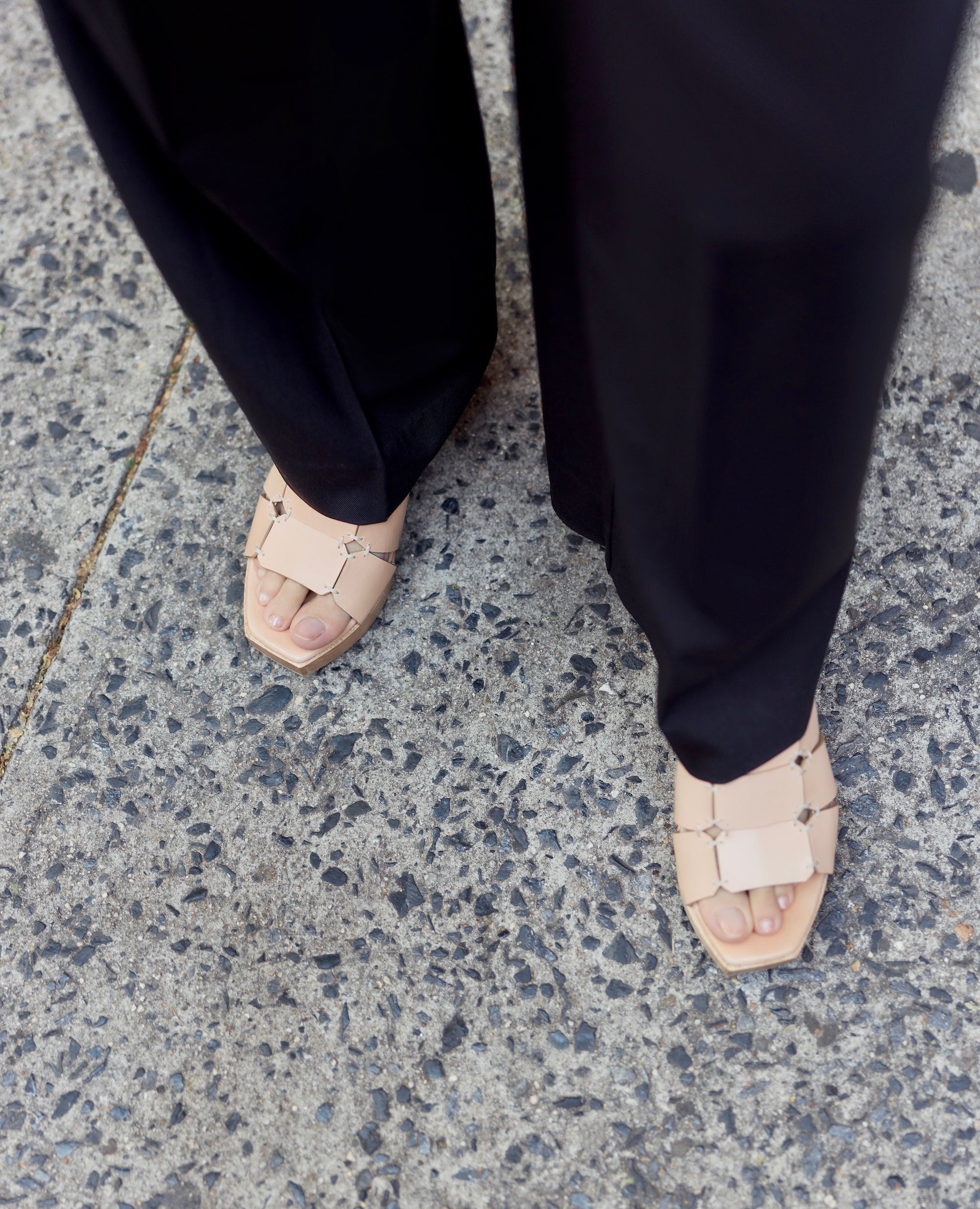 Person wearing black pants and beige sandals on pavement.