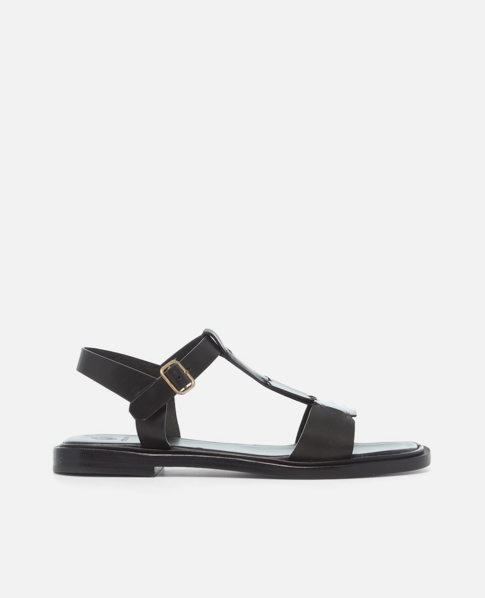 Side view of a black leather T-strap sandal with hand-linked panels, slim ankle strap, and a sleek flexible leather sole with a textured welt.