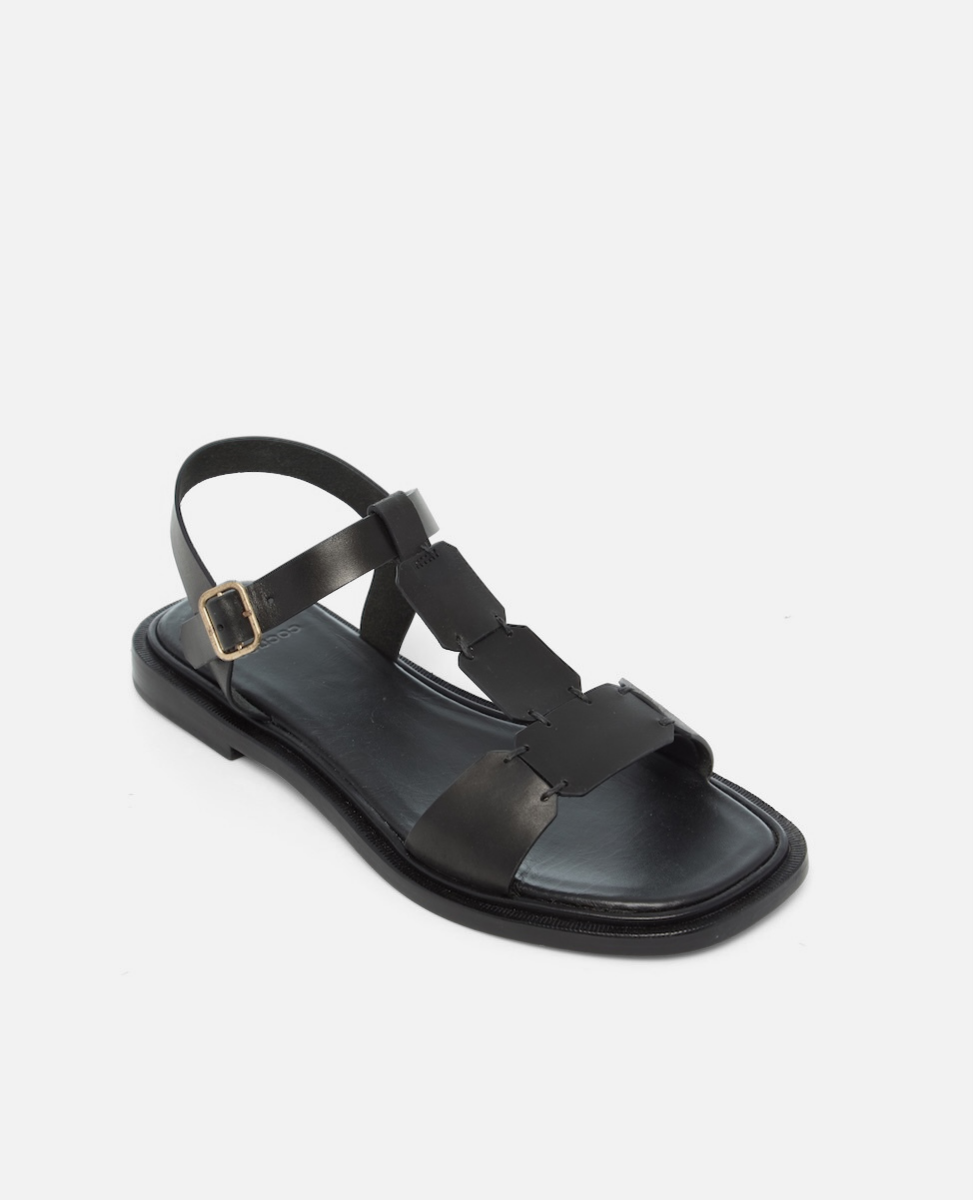 Angled view of a black leather T-strap sandal with hand-linked panels, slim ankle strap, and a sleek flexible leather sole with a textured welt.
