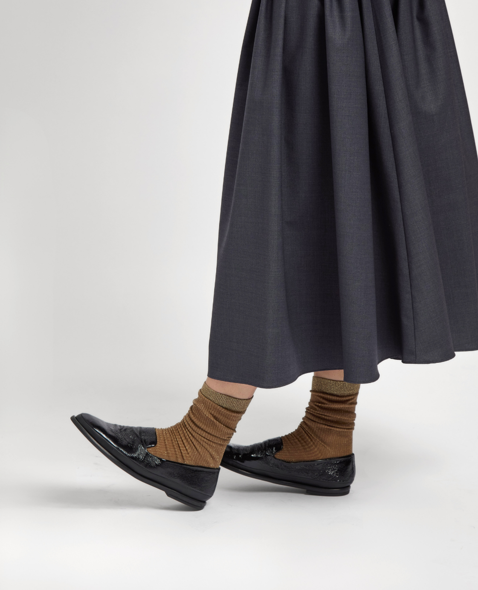 Shiny black leather loafers with a sleek, low-profile design, paired with ribbed brown socks and a long, dark gray skirt.