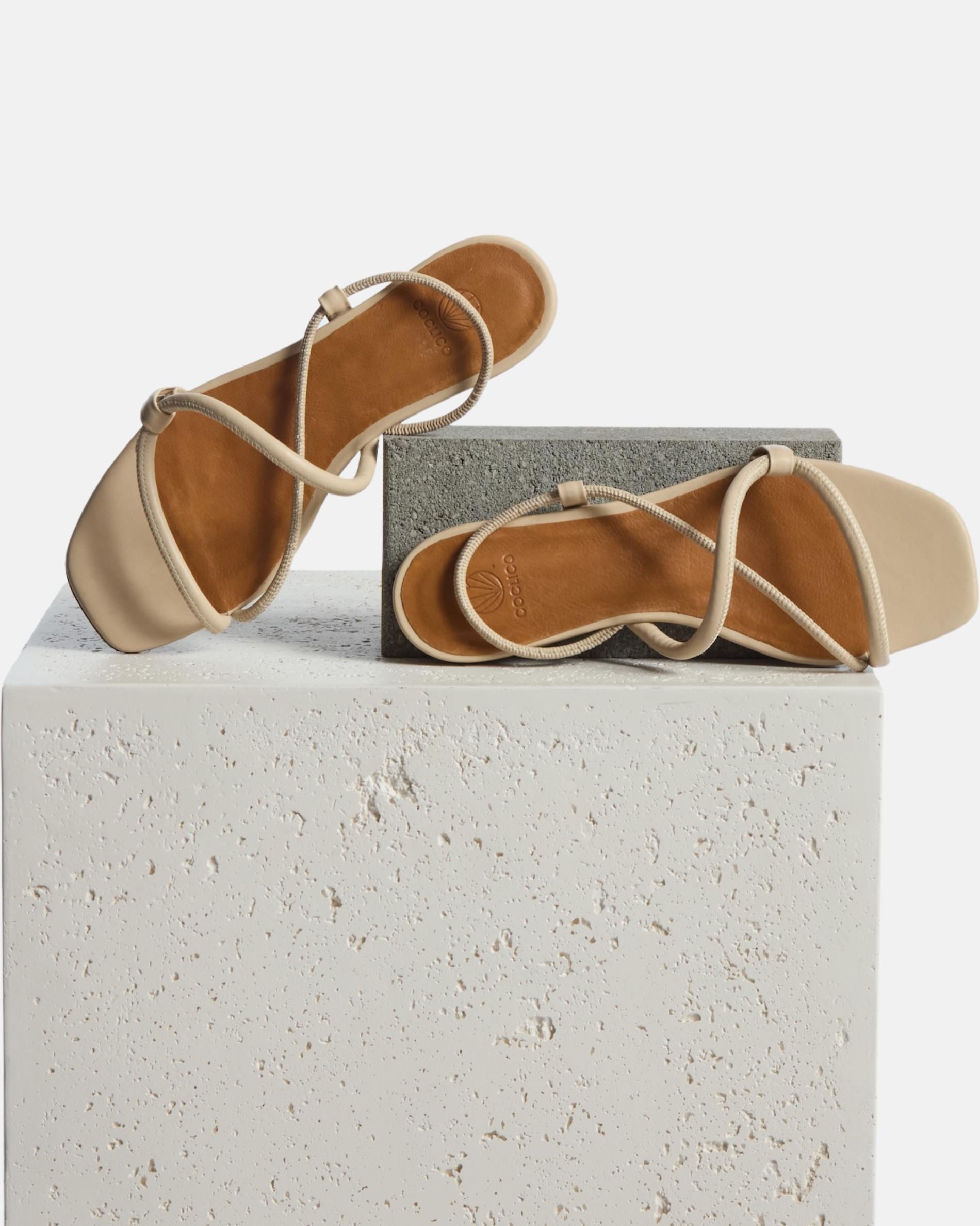 Shoe on Plinth: off-white leather flat sandal with slim padded straps, elasticated slingback, and a square toe on a white background