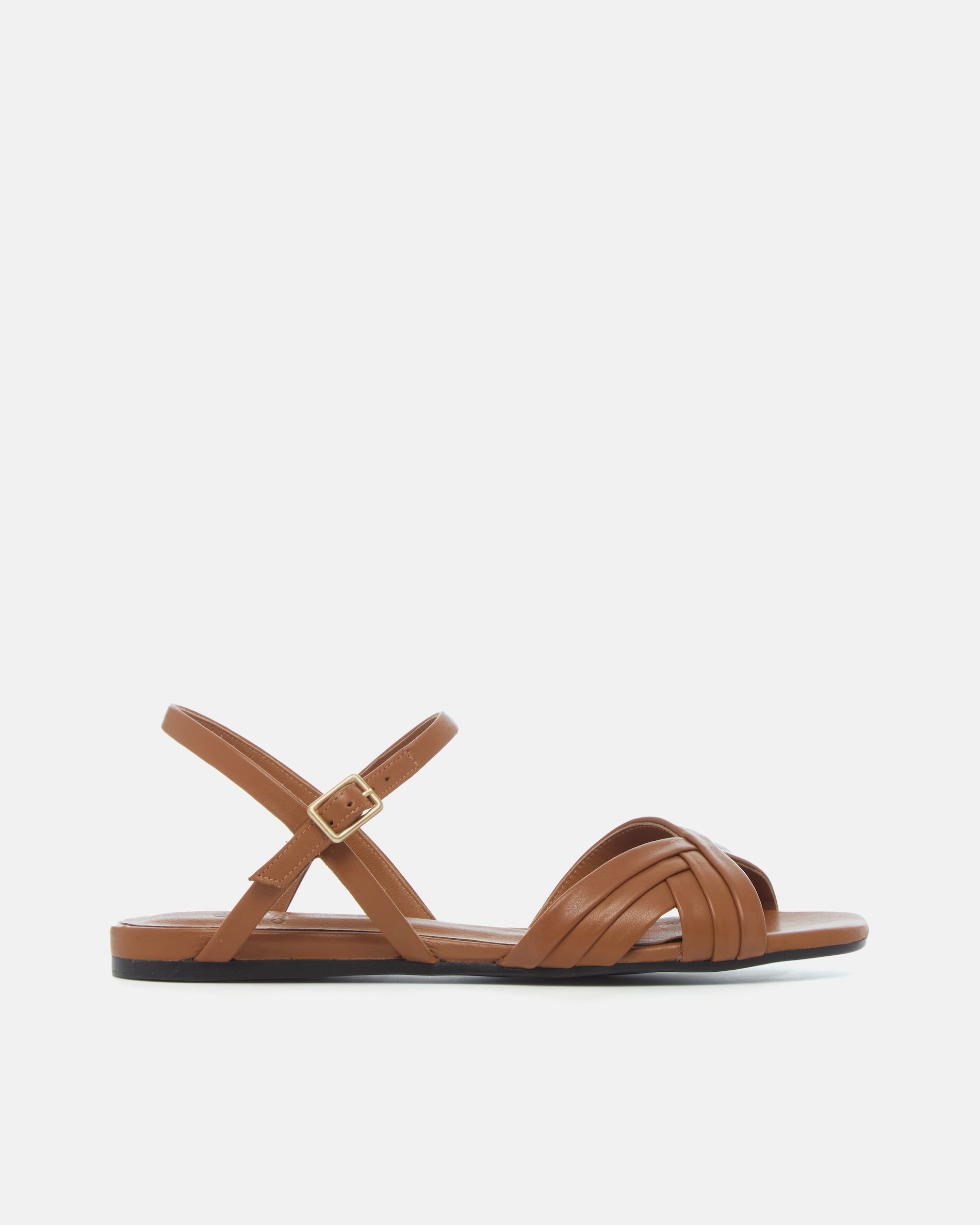 Side view of a warm brown leather sandal with slim crisscross straps, buckle quarter strap, and a square toe on a grey background