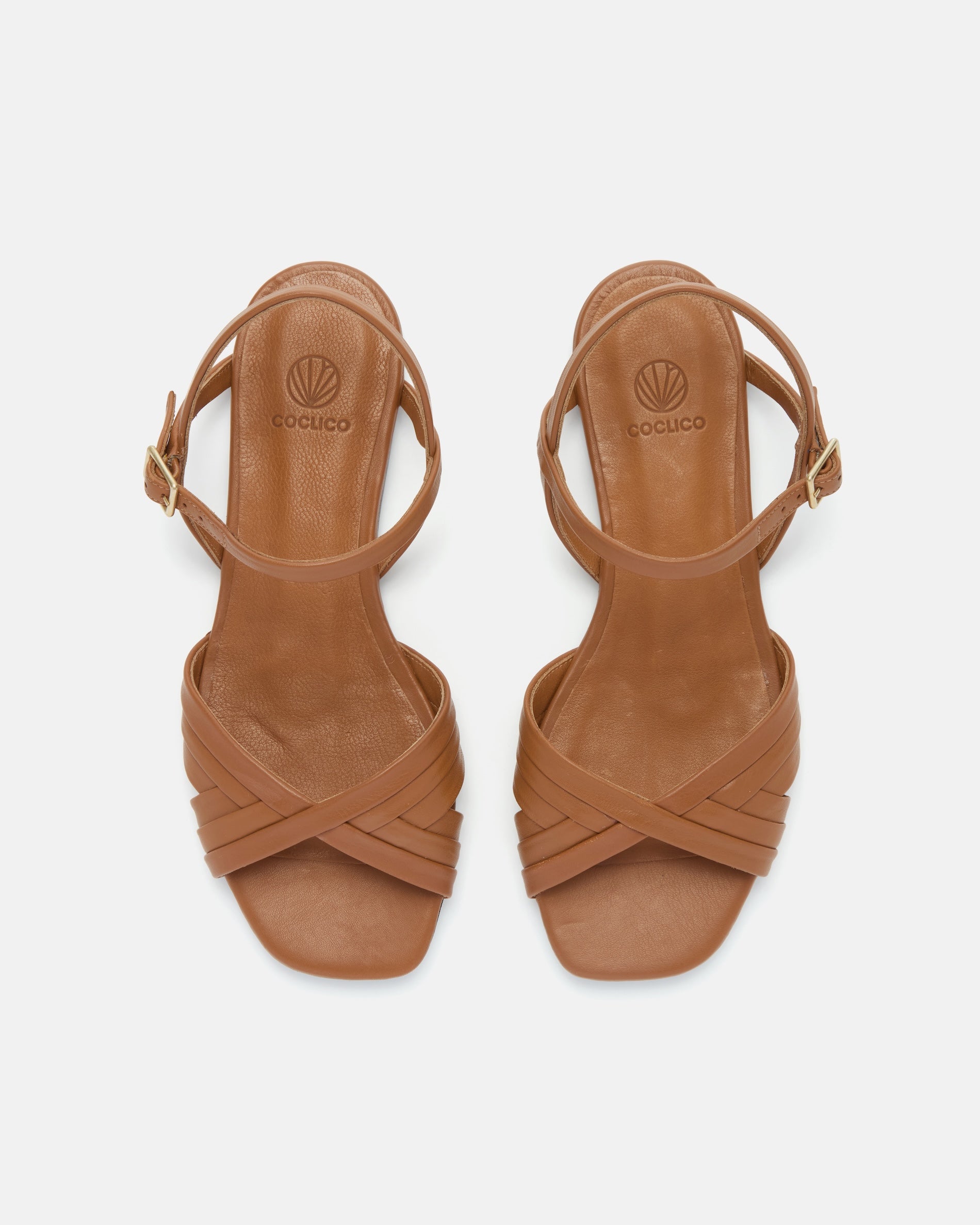 Top view of a warm brown leather sandal with slim crisscross straps, buckle quarter strap, and a square toe on a grey background