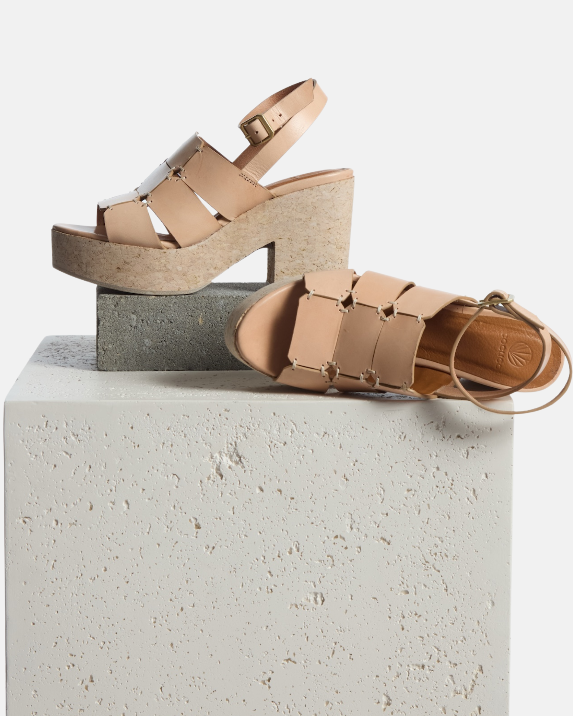 Shoe on plinth: natural vachetta leather platform sandal with octagonal cage straps, hand-stitched detailing, slim ankle strap with buckle, and a solid cork heel and platform, on a white background.