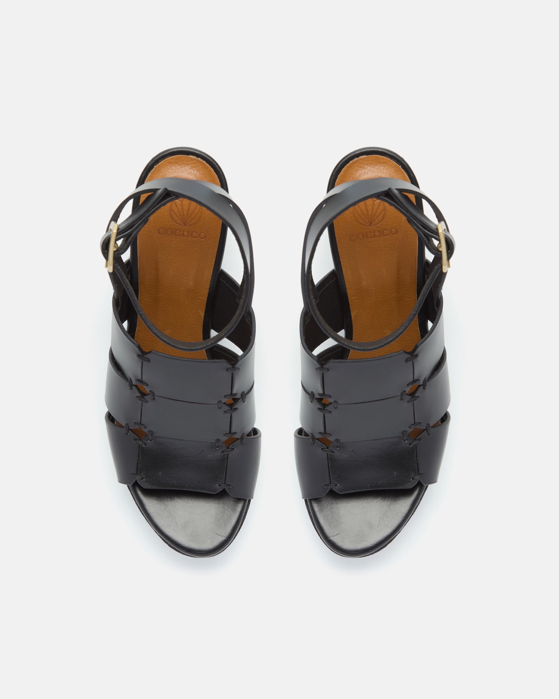 Top view of a black vachetta leather platform sandal with octagonal cage straps, hand-stitched detailing, slim ankle strap with buckle, and a solid cork heel and platform, on a white background.
