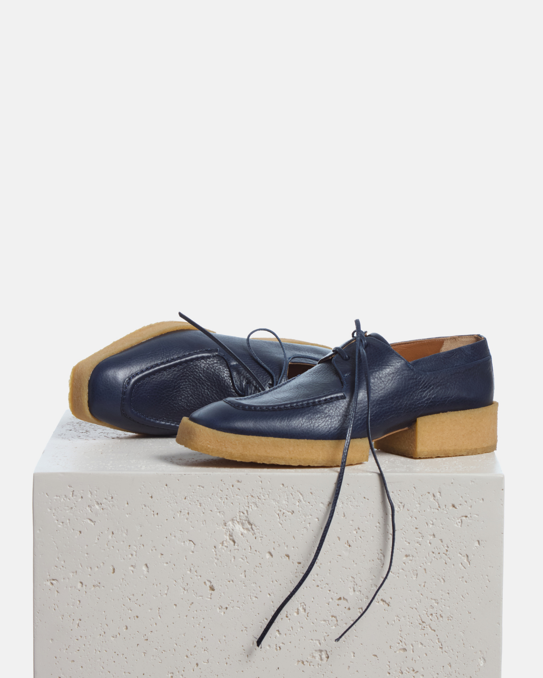 Coclico Butler Oxford in Marino, navy leather lace up oxfords with natural crepe soles styled on a stone plinth