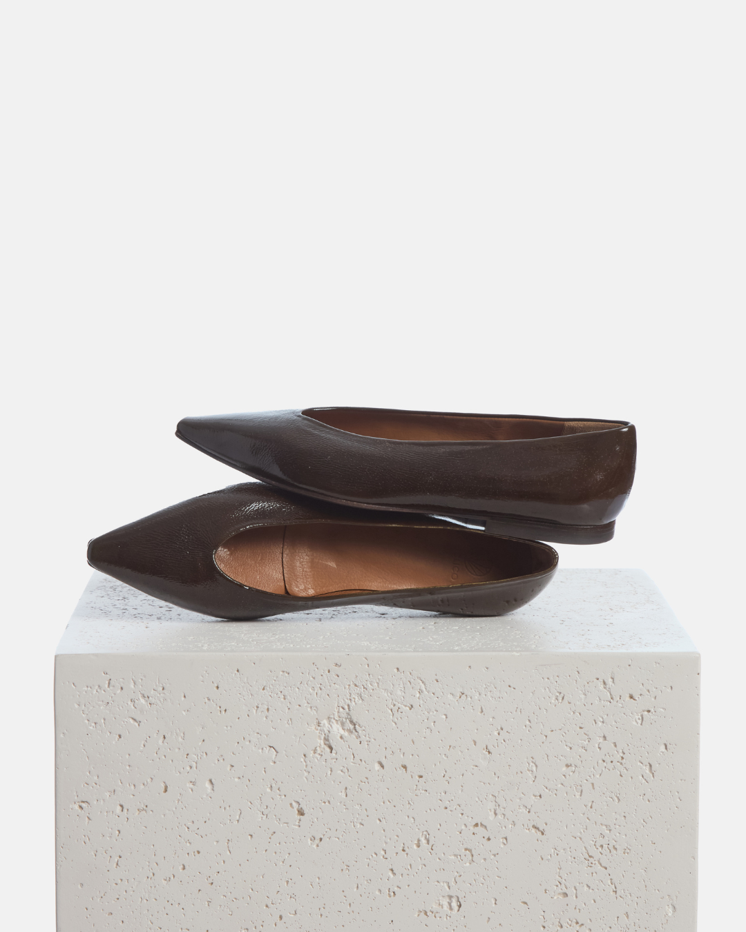 Coclico Cabnal Ballet Flat in Moule crinkled patent, dark brown pointed toe flats styled on a stone plinth
