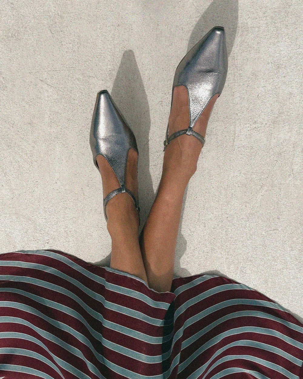 Woman wearing silver metallic t-bar pointed ballet flat shoes and a stripped skirt