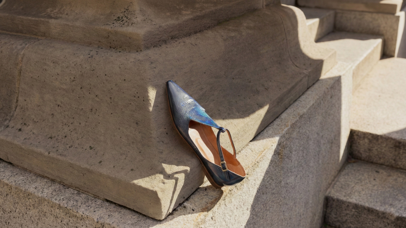 The Coclico best selling Celeste flat in Carbon blue metallic rests on the side of a building's exterior