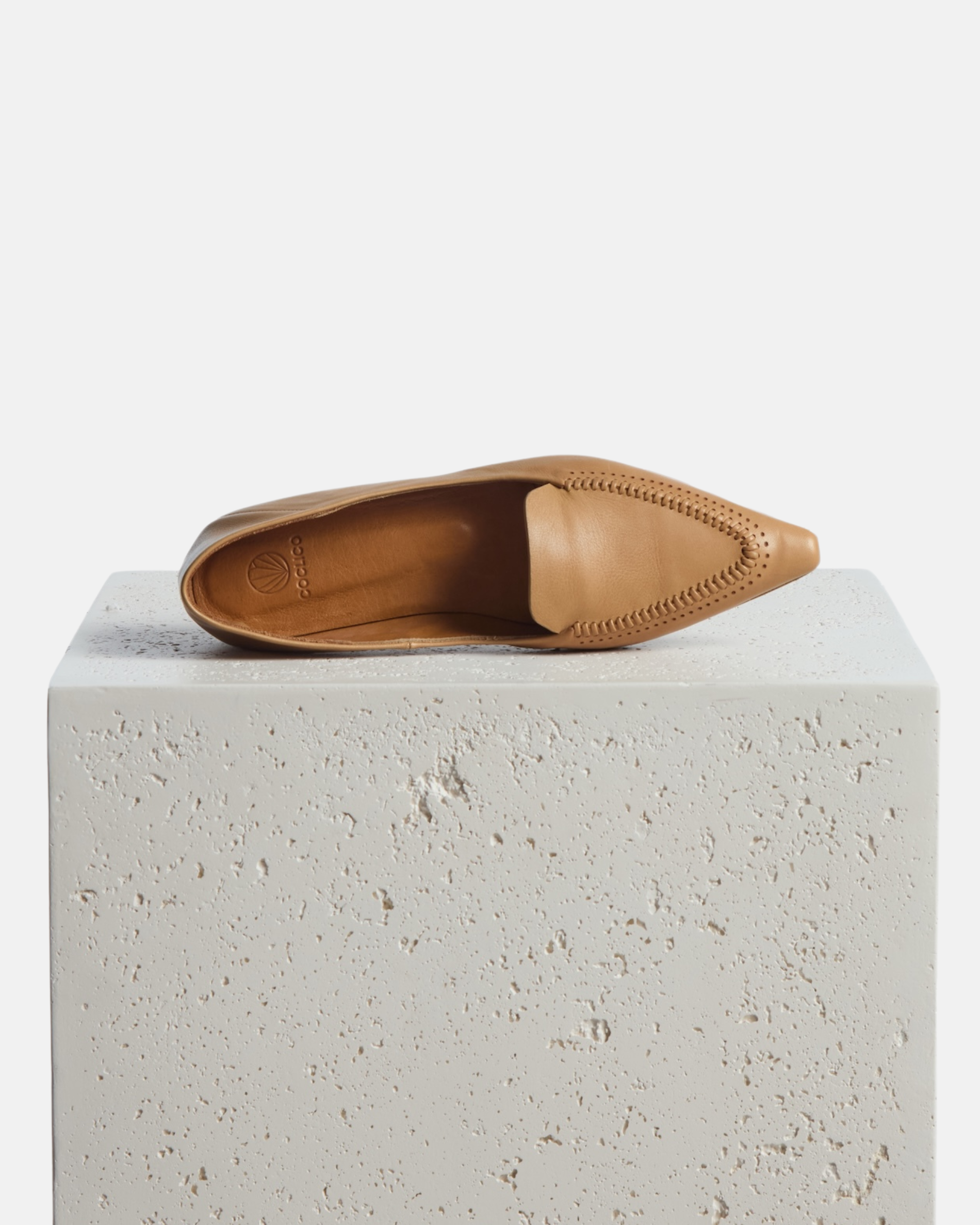 Shoe on a pedestal: pointed-toe camel leather loafer with topstitch detailing and a flat leather sole on a white background