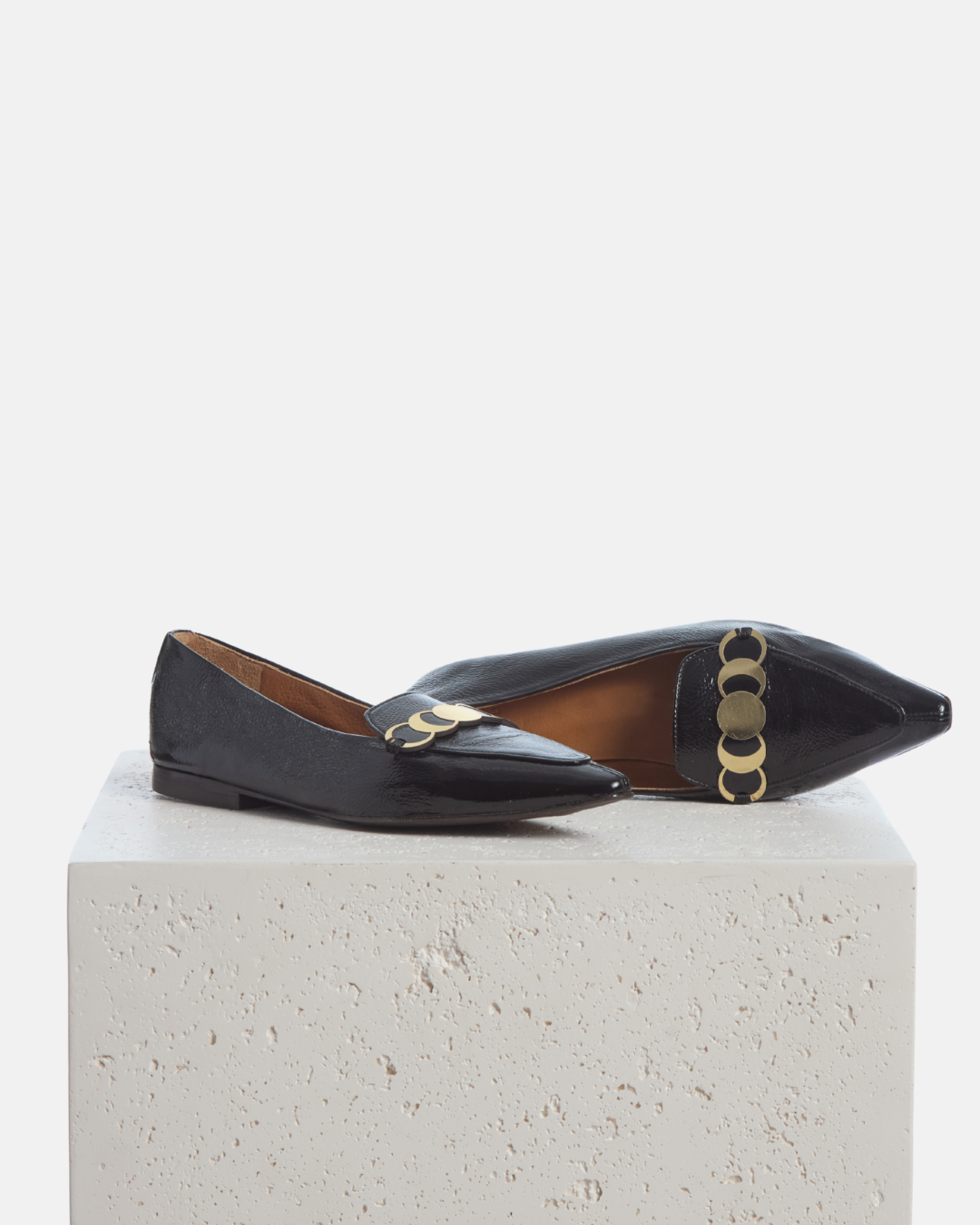 Coclico Curie Loafer in black crinkled patent, pointed toe loafers with gold coin hardware styled on a stone plinth
