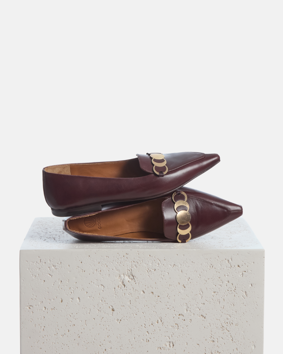 Coclico Curie Loafer in Oxblood leather, pointed toe loafers with gold coin hardware styled on a stone plinth
