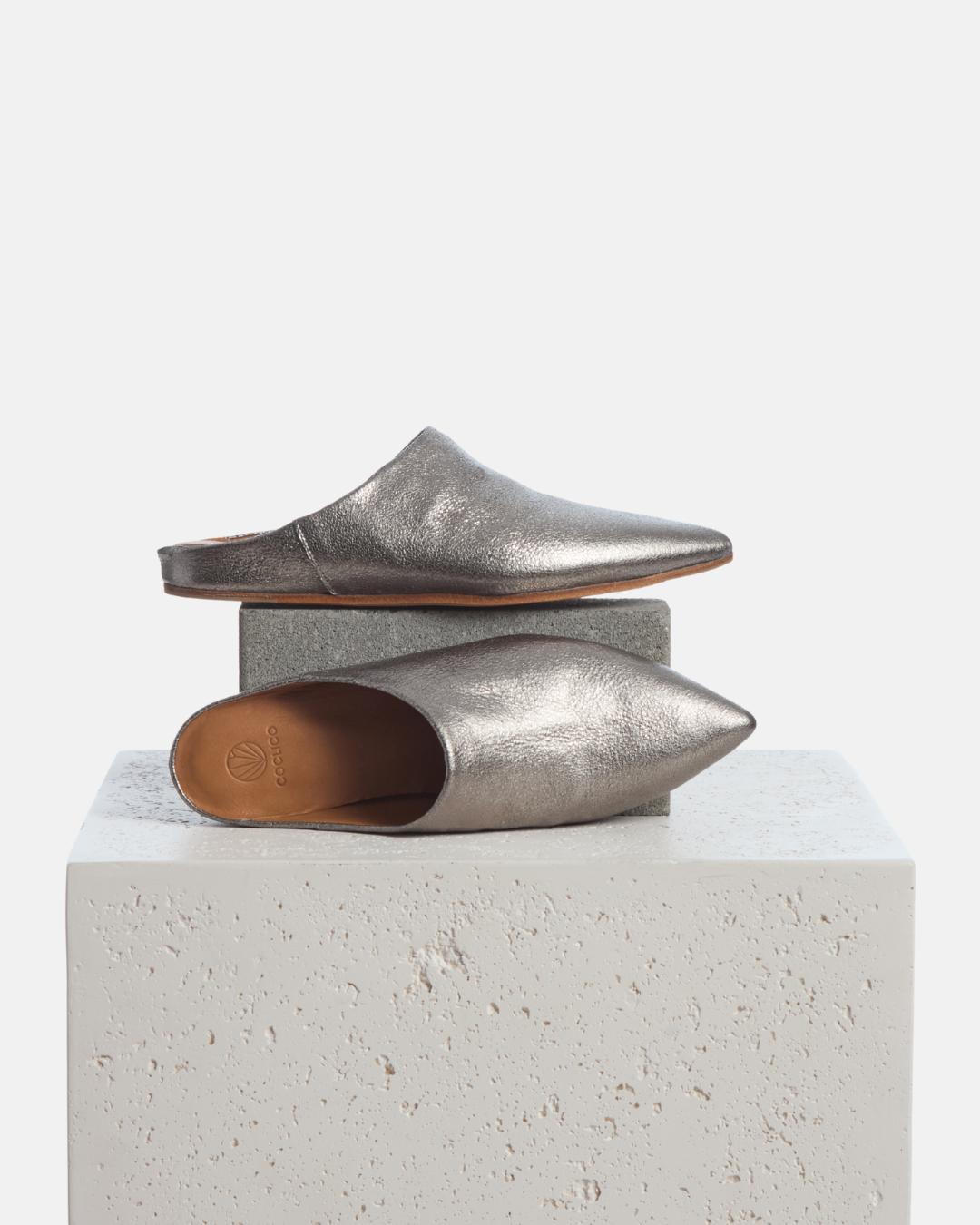 Coclico Danke Slide in Acero, silver metallic pointed toe mules styled on a stone plinth