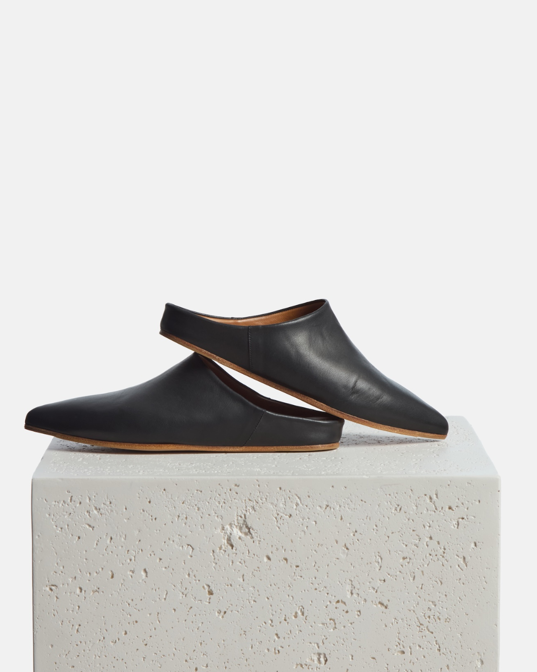 Shoes on a stone pedestal: black pointed-toe leather mule with a slight built-in wedge and clean minimalist silhouette on a white background