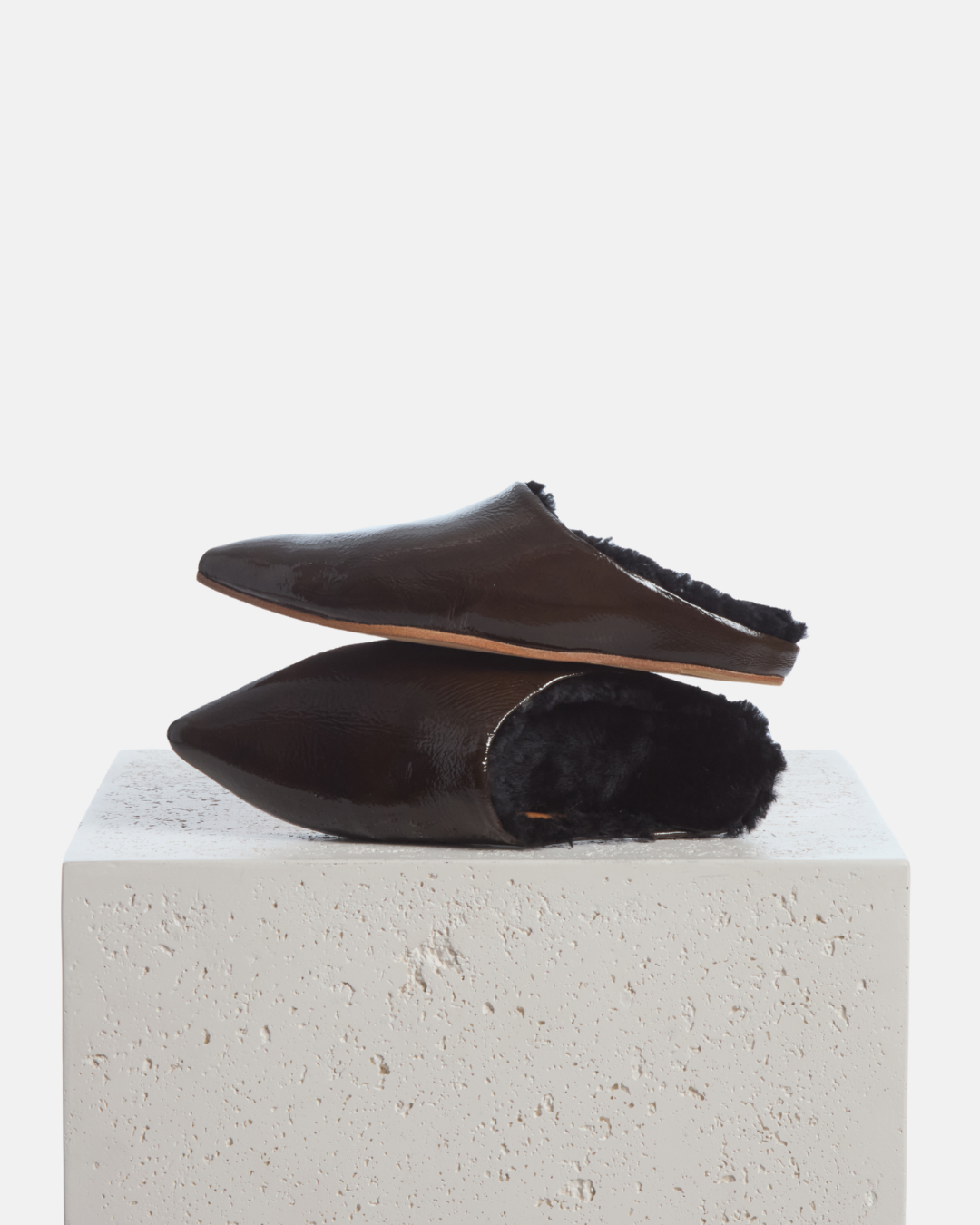Coclico Dia Shearling Slide in Moule crinkled patent, shearling lined mules styled on a stone plinth