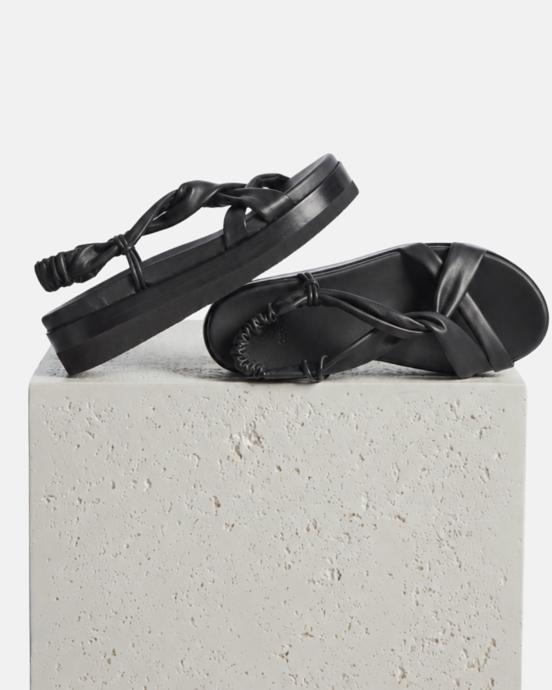 Black Coclico tubular leather sandals with a platform sole arranged on a plinth