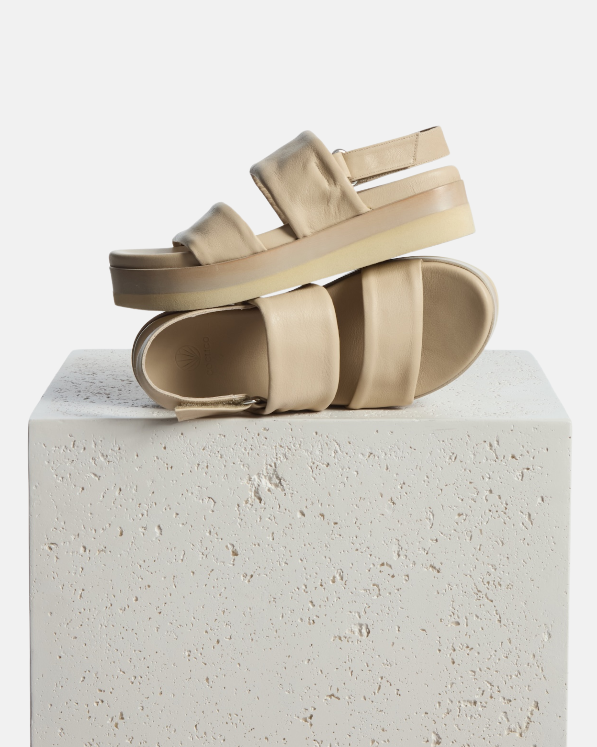 Shoe on a plinth: off-white leather wedge sandal with wide tubular straps, velcro slingback, and a lightweight EVA platform sole