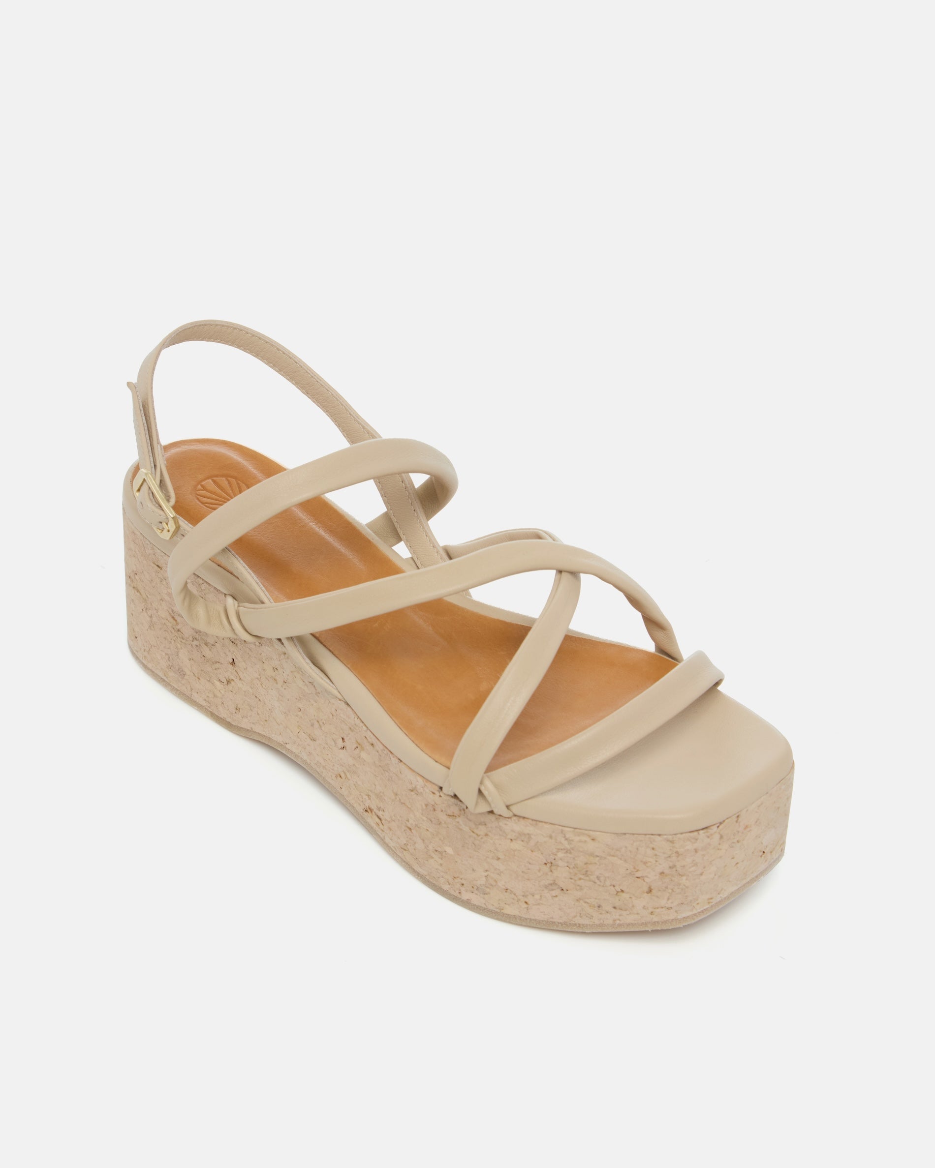 Angled view of a off-white leather cork wedge sandal with slim crisscross straps, adjustable slingback, and a sculptural cork platform sole