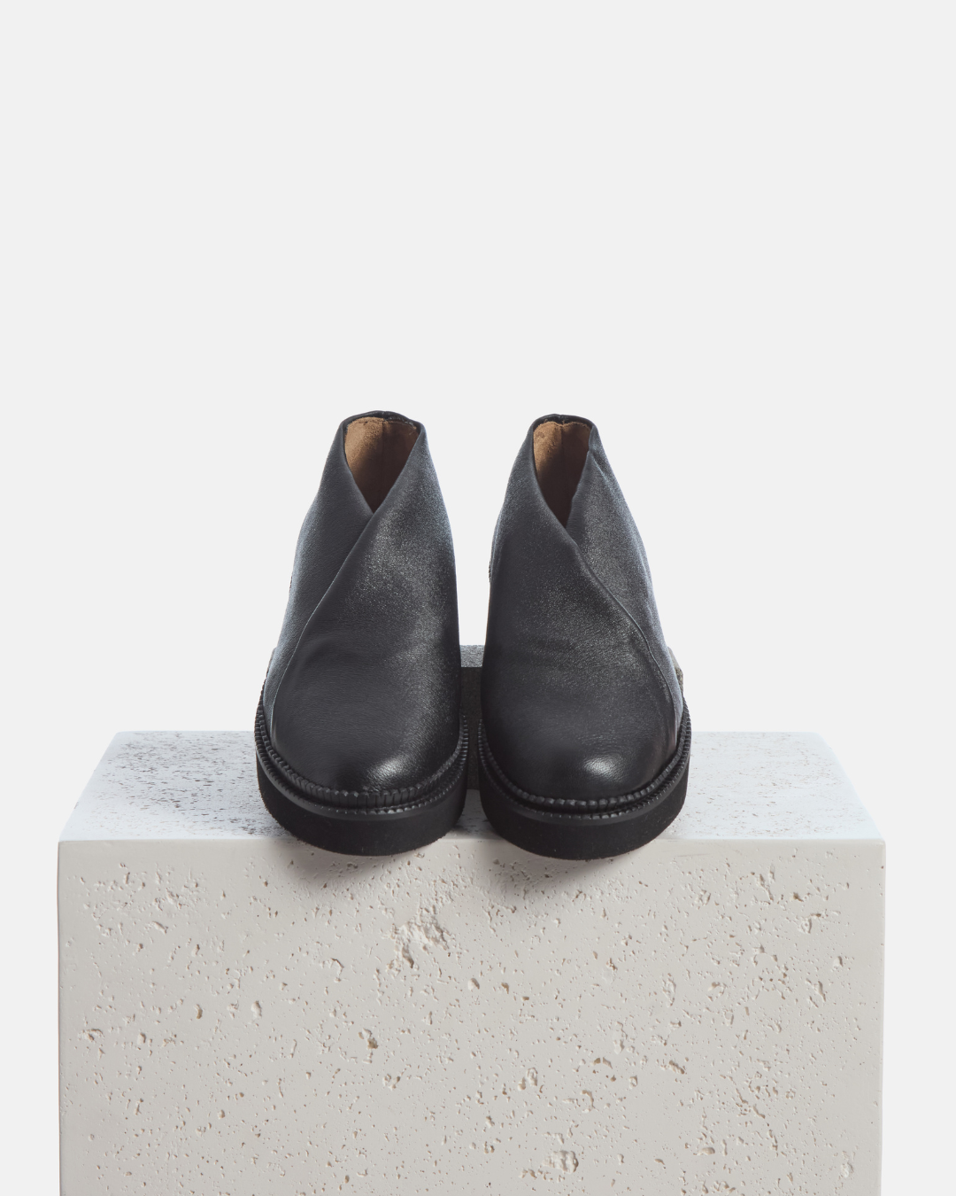 Coclico Grace Flatform in black stretch leather, crossover slip ons styled on a stone plinth