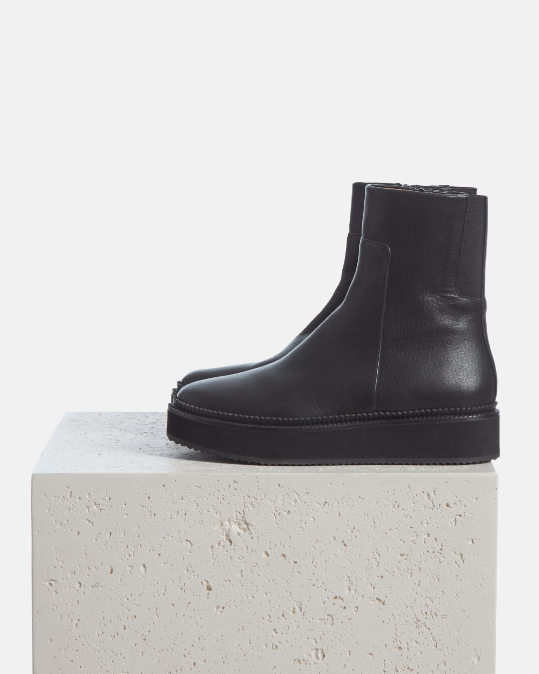 Coclico Greta Boot in black leather, platform ankle boots with back zips styled on a stone plinth