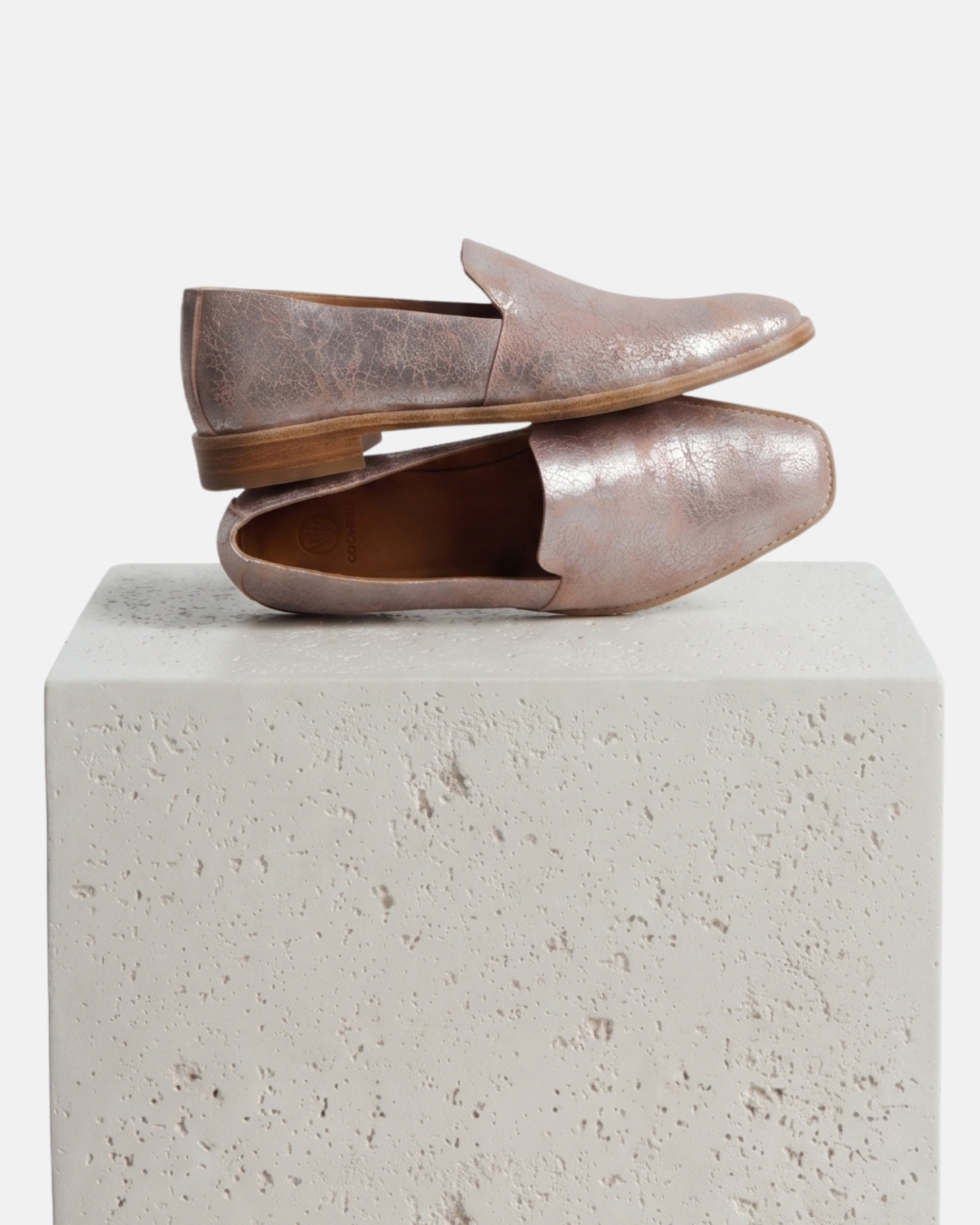 Pair of pink metallic loafers on a plinth
