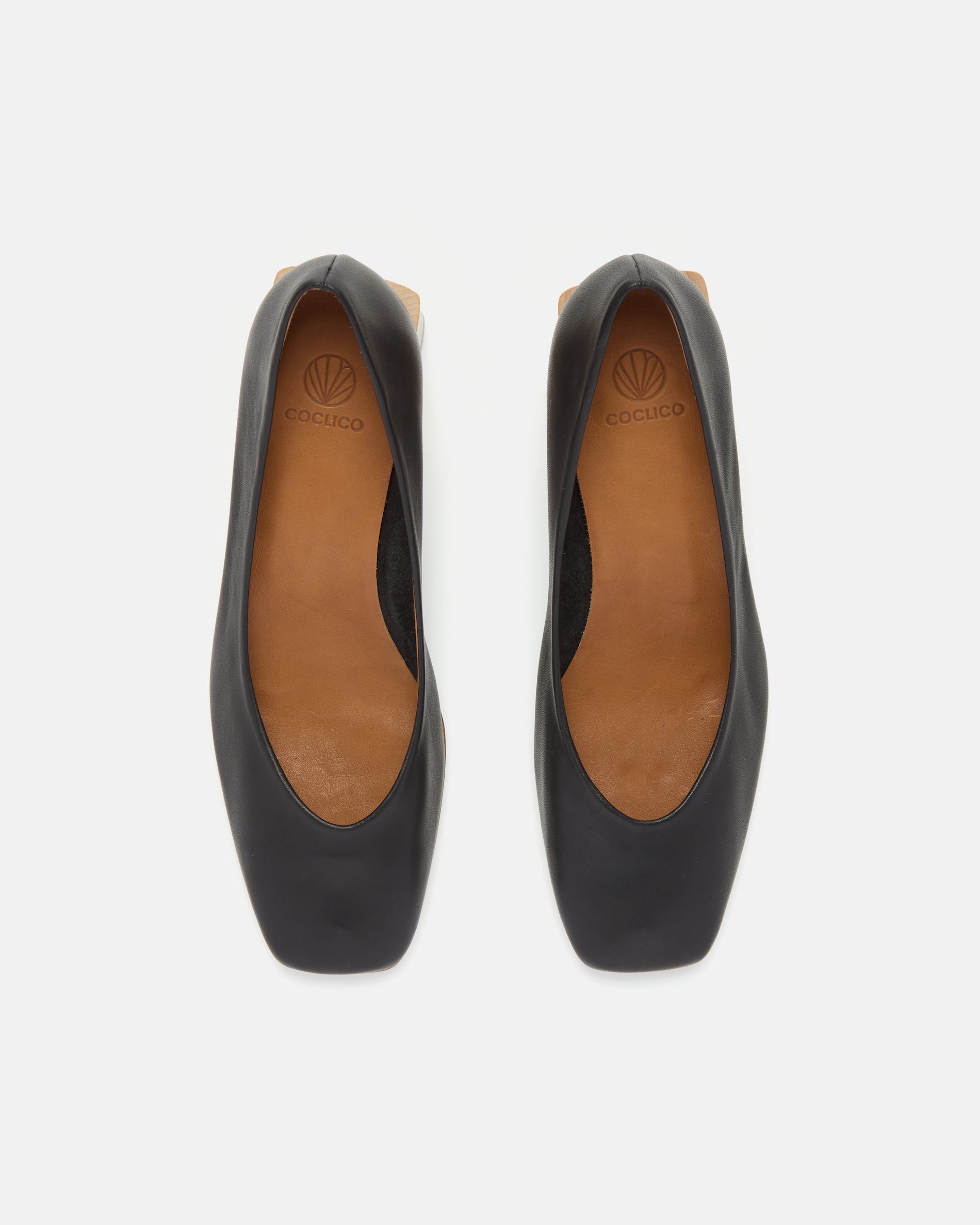 Top view of pair of black mid-heeled shoes with a sculpted square toe with tan insoles on a white background