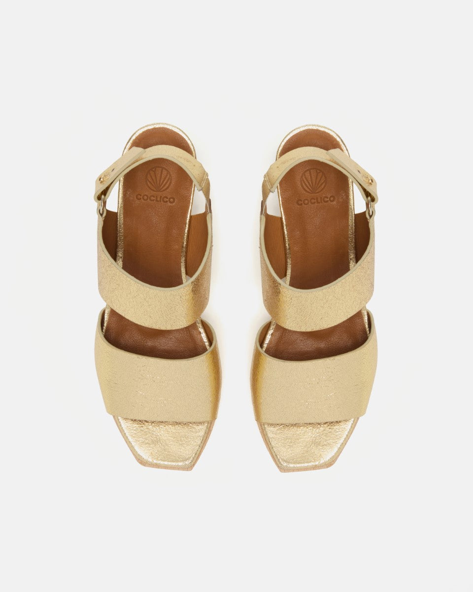 Front view of gold leather clog sandal with wide straps, adjustable slingback, squared toe, and solid ash wood block heel on a white background.