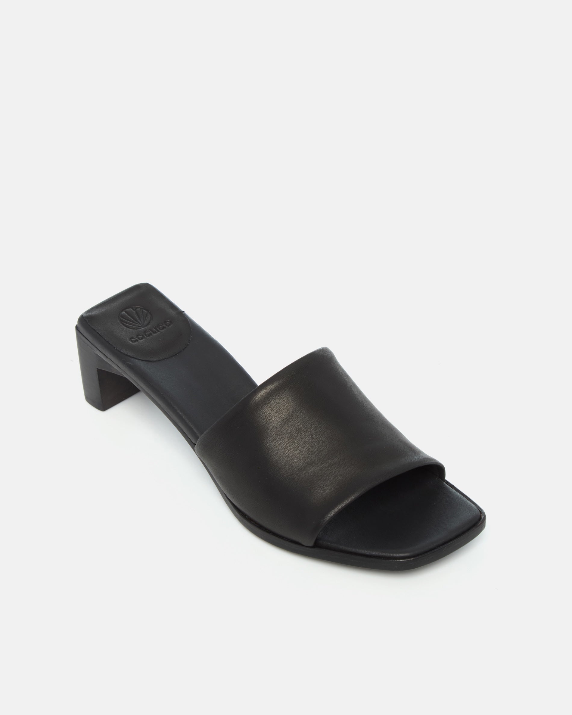 Angled view of a black leather sandal with a wide band, squared toe, and sculptural wooden block heel