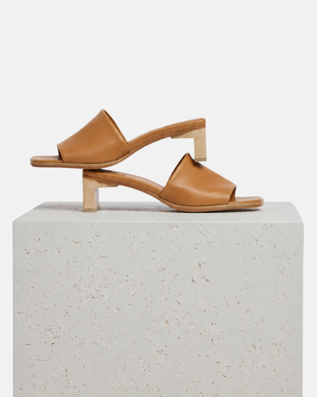 Wood mid-heel slide sandal in tan leather arranged on a white plinth