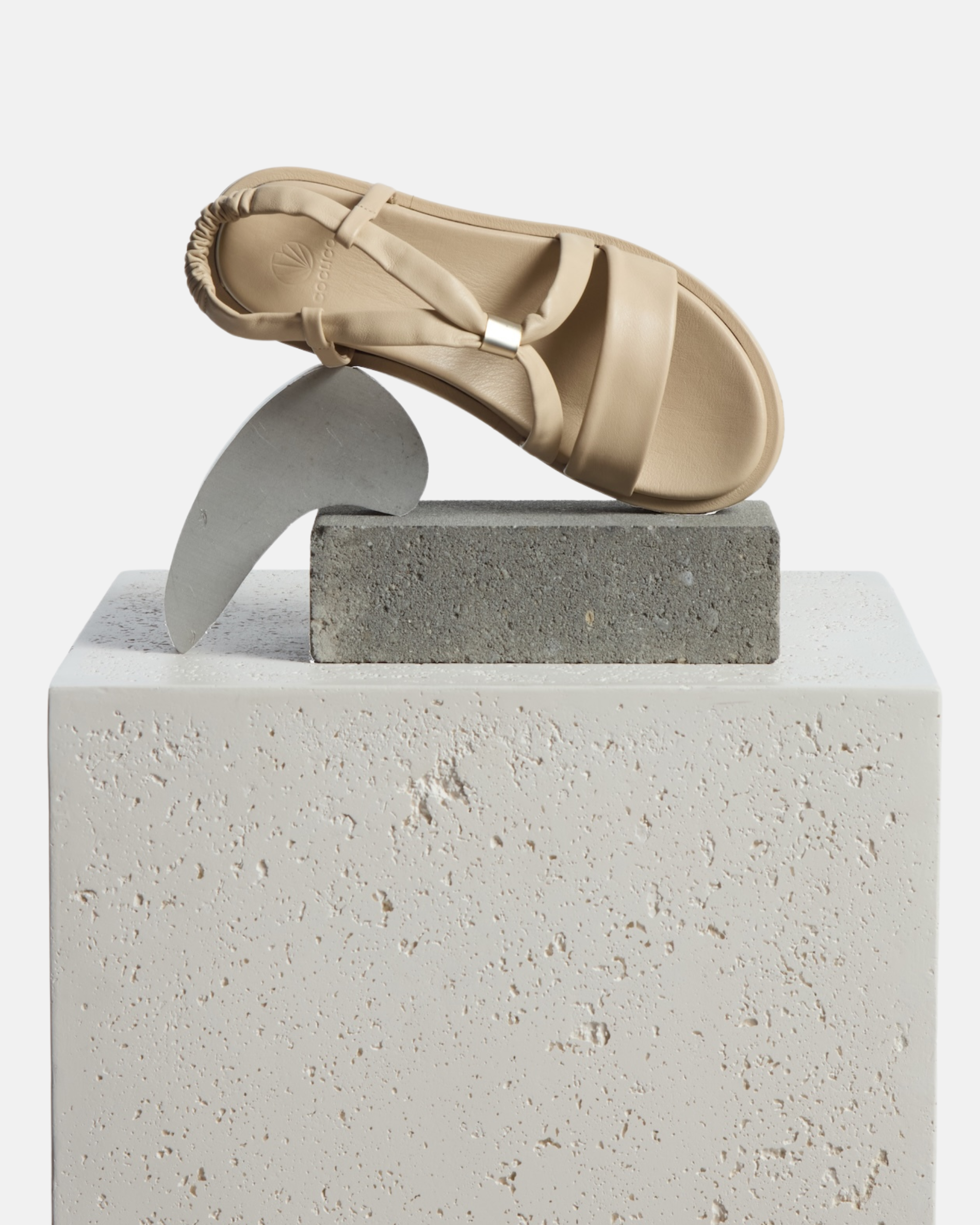 A shoe arranged on a plinth: milky white leather slingback footbed sandal with soft tubular straps, brushed-metal keeper detail, and a cushioned platform sole on a white background